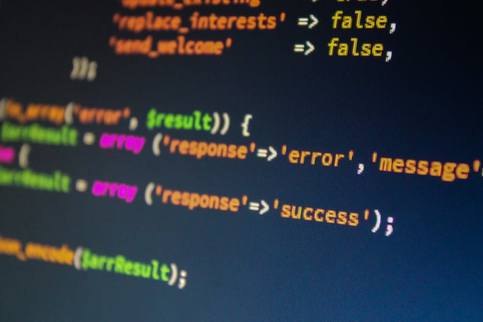 Close-up of a computer screen displaying colorful lines of programming code in a dark-themed editor. The code includes keywords and syntax highlighted in orange, green, pink, and yellow, with the word