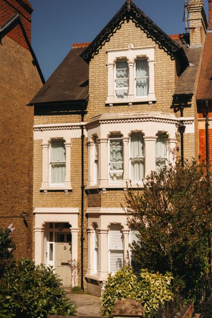 Exterior view of a modern Twickenham terrace house featuring a light pink facade with white window frames and small balconies with black railings. The ground level shows a paved driveway with a garage